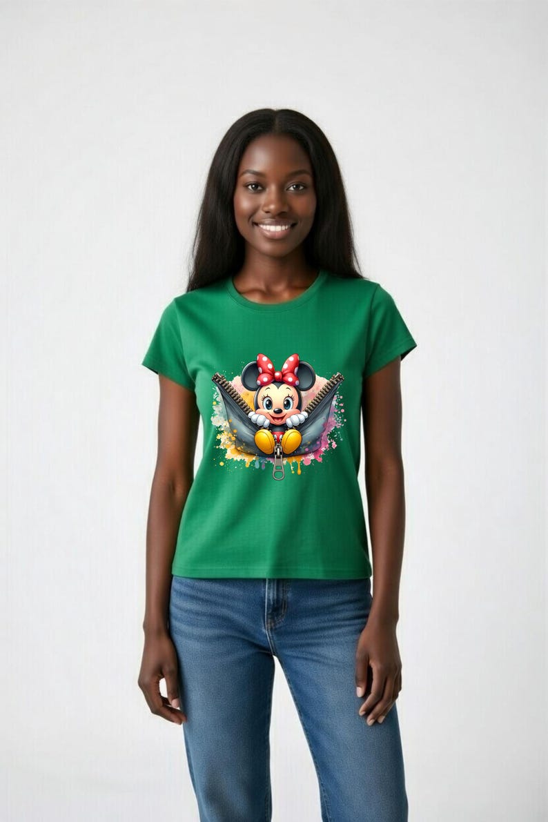 May include: Green t-shirt featuring a graphic of Minnie Mouse peeking out of a zipper. The cartoon character has a red bow and yellow shoes. The zipper is black with a gold-colored pull. The background has colorful paint splatters.