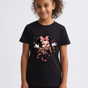 May include: Black t-shirt featuring a cartoon Minnie Mouse design. Minnie Mouse is wearing a leopard print jacket and bow, with pink accents. The design includes stars and sparkles. The shirt is worn by a young person.