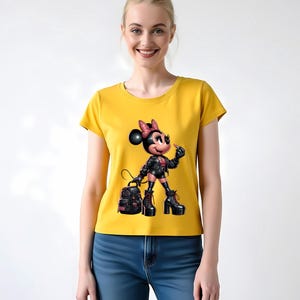Peut inclure: T-shirt jaune moutarde avec un dessin de souris de dessin anim&eacute; portant une veste en cuir noire, des bottes et un sac &agrave; dos. La souris a un n&oelig;ud rose et tient une cigarette. Le t-shirt est port&eacute; avec un jean bleu.