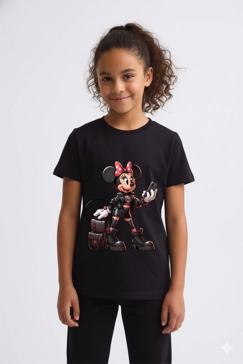 Peut inclure: T-shirt noir avec un dessin anim&eacute; de Minnie Mouse portant une veste noire, des bottes et un sac &agrave; dos. Minnie tient un t&eacute;l&eacute;phone et porte un n&oelig;ud rouge. Le fond est blanc.