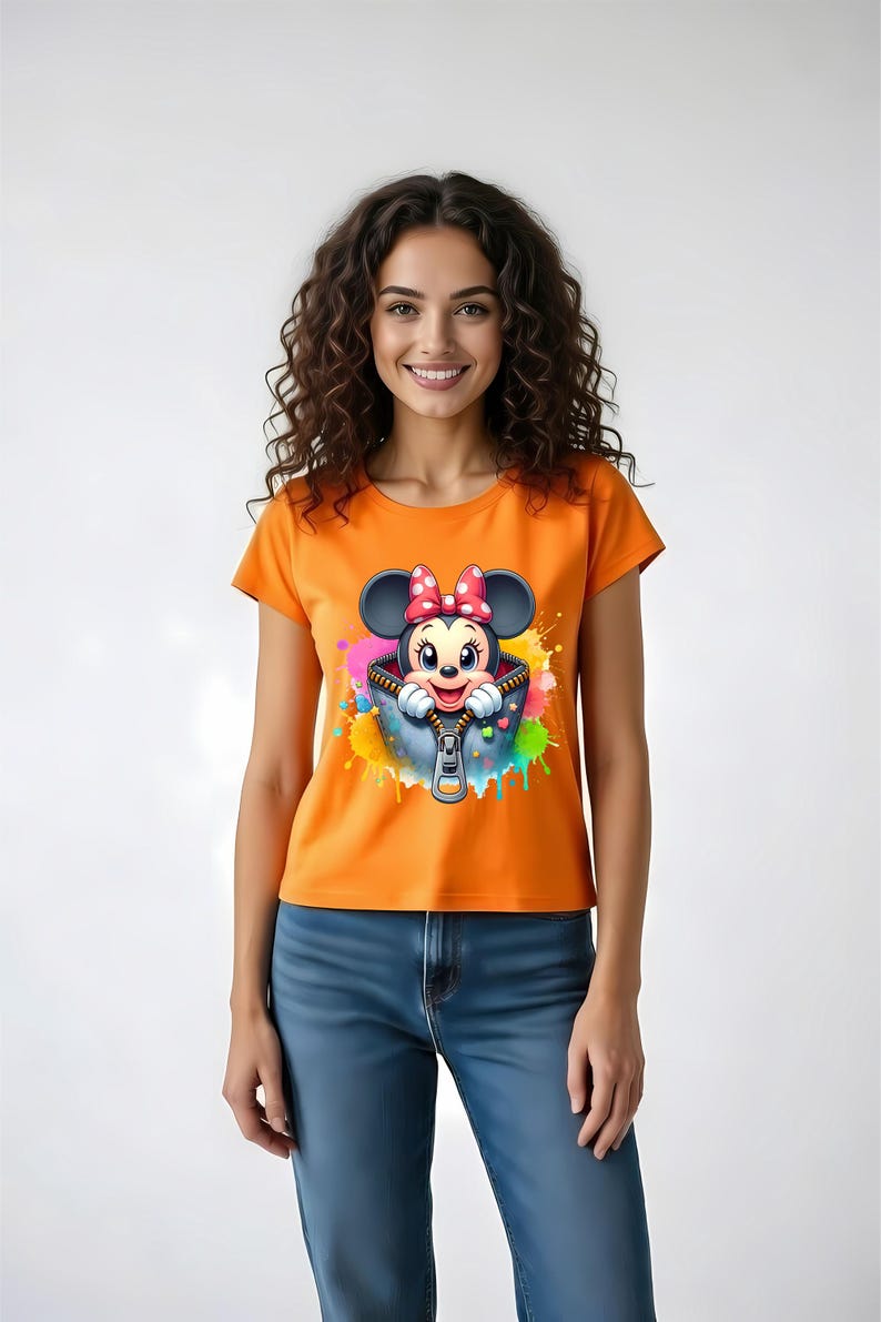 May include: Orange t-shirt featuring a cartoon Minnie Mouse design. The graphic shows Minnie peeking out of a zippered pocket with colorful paint splatter accents. The shirt is paired with blue jeans.
