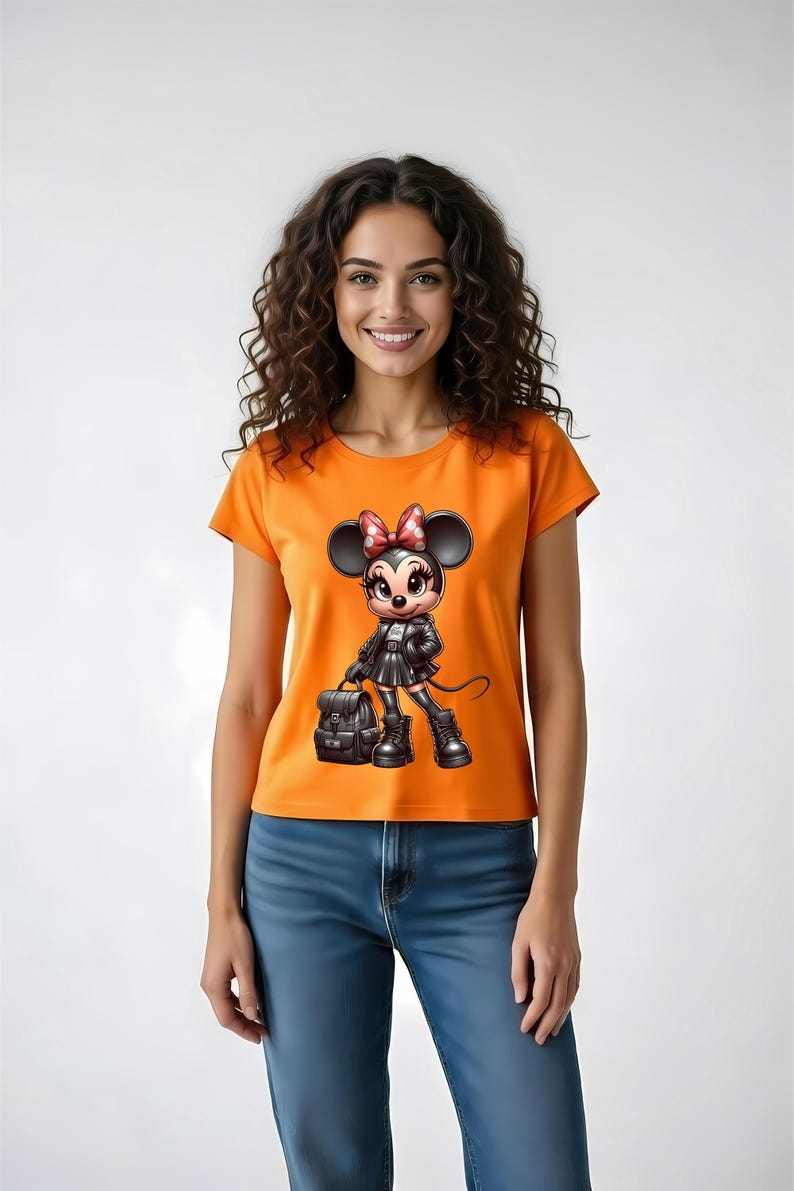 Peut inclure: T-shirt orange avec un personnage de dessin anim&eacute; Minnie Mouse en tenue noire, tenant un sac &agrave; dos. Le personnage a un n&oelig;ud rouge &agrave; pois blancs. Le mod&egrave;le porte un jean bleu.