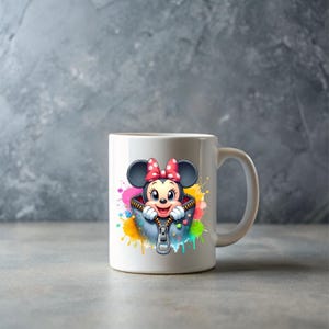 May include: White ceramic mug featuring a cartoon Minnie Mouse design. Minnie Mouse is wearing a red bow and is inside a zippered jacket with colorful paint splatter accents. The mug has a curved handle.