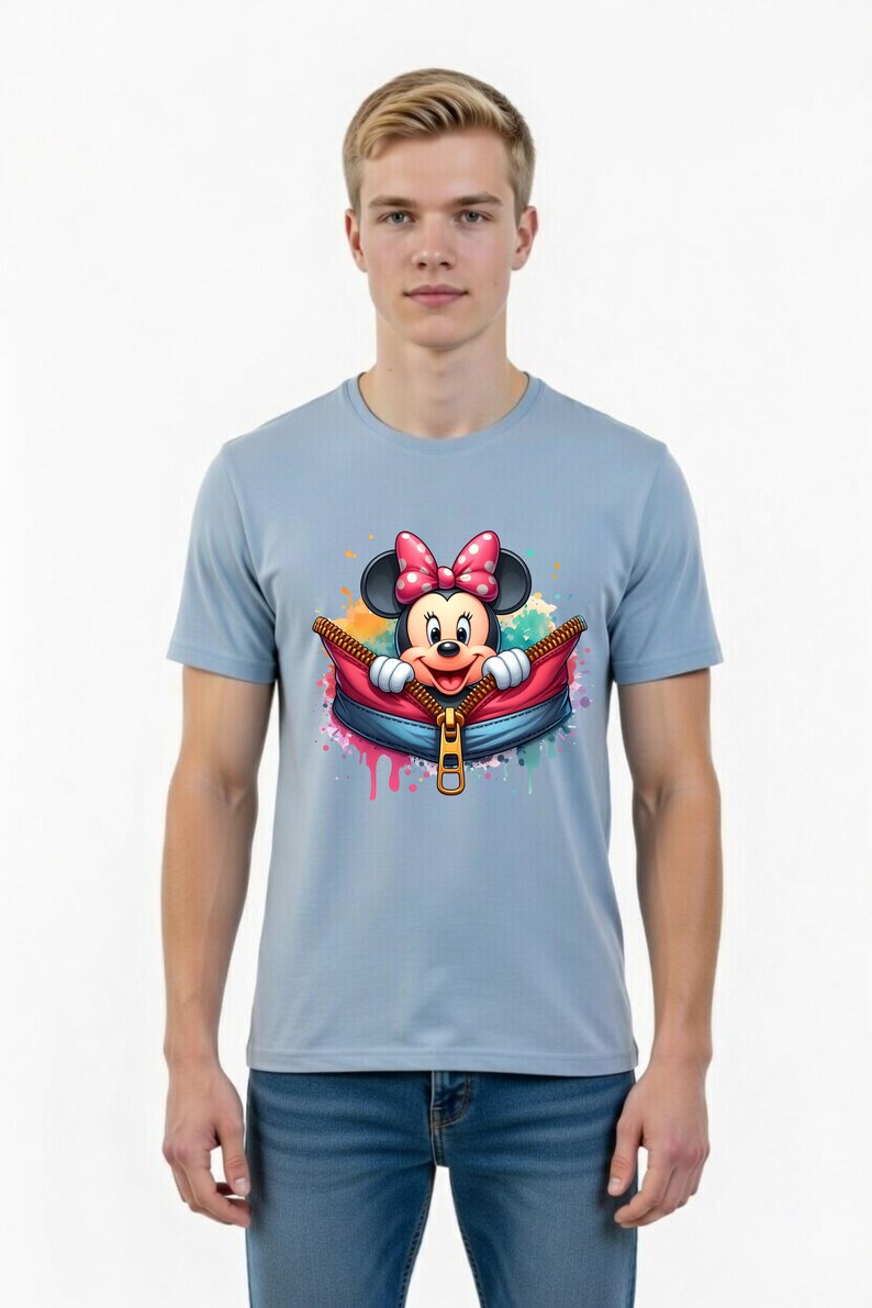 May include: Light blue t-shirt featuring a colorful graphic of Minnie Mouse emerging from a zippered pouch. Minnie Mouse is wearing a pink polka-dot bow. The design includes colorful paint splatters.