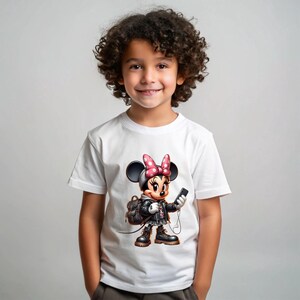 Peut inclure: T-shirt blanc avec un dessin anim&eacute; de Minnie Mouse portant une veste en cuir noire et tenant un smartphone. Le design comprend un n&oelig;ud rose et un sac &agrave; dos. Le t-shirt est port&eacute; par un enfant.