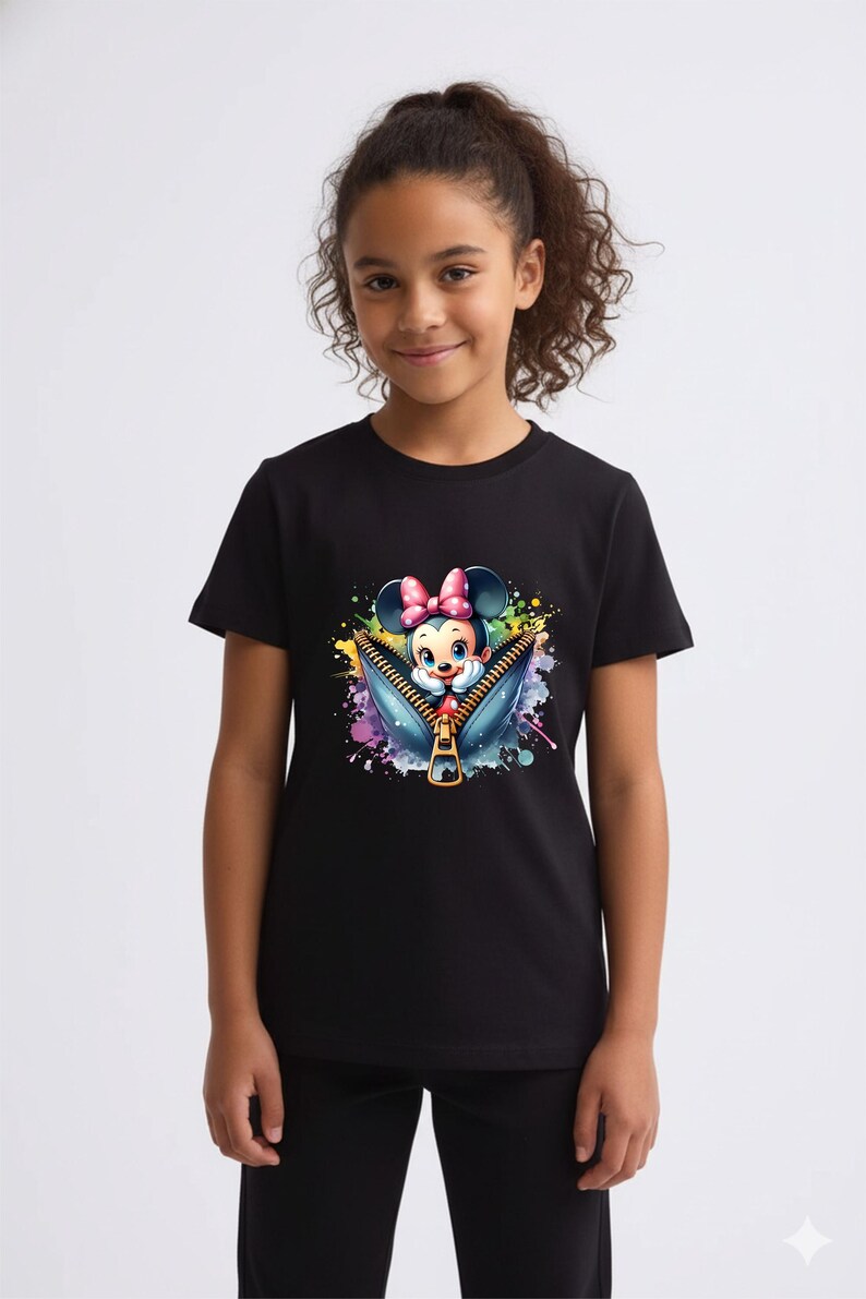 May include: Black t-shirt featuring a colorful graphic of Minnie Mouse emerging from a zipper. The design includes a pink bow, blue eyes, and a vibrant splash of watercolor-style paint. The shirt is worn by a young person.