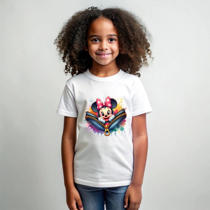 May include: White t-shirt featuring a colorful graphic of Minnie Mouse peeking out of a zipper. The design includes a pink bow, and the zipper is surrounded by paint splatters. The shirt is worn by a young girl.