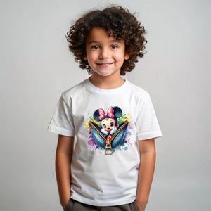 May include: White t-shirt featuring a colorful graphic of Minnie Mouse emerging from a denim zipper. The design includes a pink bow, and a splash of watercolor paint. The shirt is worn by a young child.