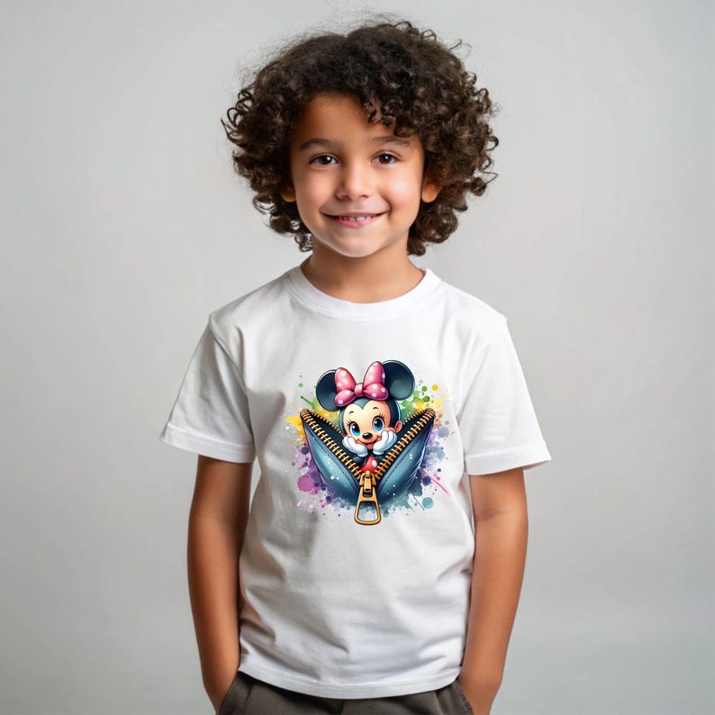 May include: White t-shirt featuring a colorful graphic of Minnie Mouse emerging from a denim zipper. The design includes a pink bow, and a splash of watercolor paint. The shirt is worn by a young child.