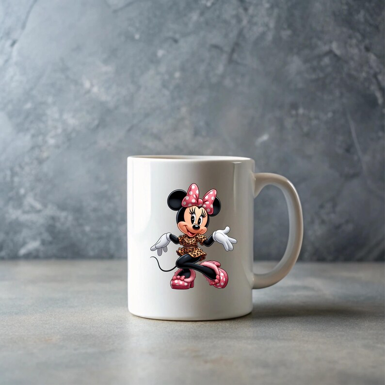 May include: White ceramic mug featuring a cartoon illustration of Minnie Mouse. Minnie Mouse is depicted in a leopard print dress, pink polka dot bow, and shoes. The mug has a curved handle and is set against a gray background.