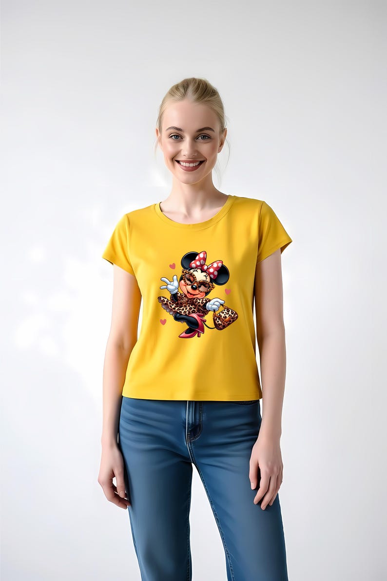 May include: Mustard yellow t-shirt featuring a cartoon Minnie Mouse in a leopard print outfit, red bow, and sunglasses. The graphic includes hearts and a purse. The model is wearing blue jeans.