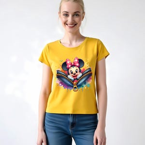 May include: Yellow t-shirt featuring a graphic of Minnie Mouse peeking out of a zipper. The zipper is blue with a gold pull, and the design includes colorful paint splatters. The shirt is worn by a person wearing blue jeans.