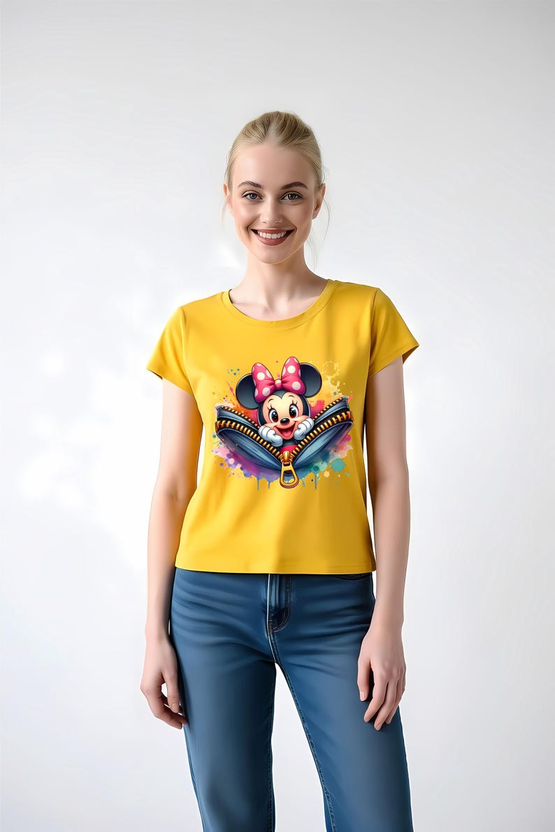 May include: Yellow t-shirt featuring a graphic of Minnie Mouse peeking out of a zipper. The zipper is blue with a gold pull, and the design includes colorful paint splatters. The shirt is worn by a person wearing blue jeans.