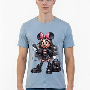 Peut inclure: T-shirt bleu clair avec une illustration de Minnie Mouse en tenue noire, tenant un t&eacute;l&eacute;phone et un sac &agrave; dos. Minnie Mouse porte un n&oelig;ud rose &agrave; pois blancs. Le t-shirt est port&eacute; par une personne.