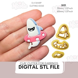 Puede incluir: Un cortador de arcilla para pendientes con forma de tiburón de dibujos animados con un flotador rosa. El tiburón es blanco y azul claro con una máscara negra. Tamaño: 35mm (1,37 pulgadas) y 40mm (1,57 pulgadas).