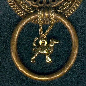 May include: A gold-toned metal door knob with a decorative design and a small gold charm of a dog hanging from it.