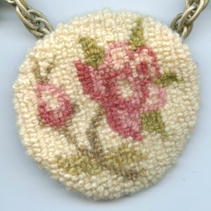 May include: A round, cream-colored needlepoint ornament with a floral design. The flowers are pink and green and are arranged in a cluster.