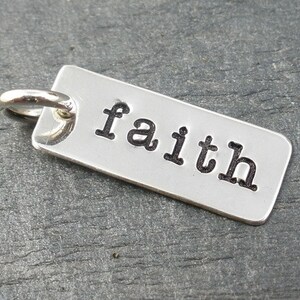 May include: Silver charm with a rectangular tag that says "faith" in a bold, black font.