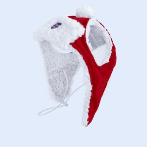 May include: A red and white winter hat with ear flaps and a pom-pom. The hat is made of a soft, plush material with a white, fuzzy lining and trim. A white drawstring is visible.