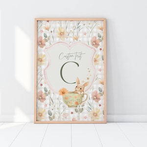 Op de afbeelding: Een printbare kinderkamerkunstprint met een konijn dat in een theekopje zit met een bloemige achtergrond en een roze-wit geruit patroon. De print bevat de letter "C" en de tekst "Custom Text".