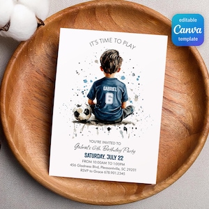 May include: A white invitation card with the text "IT'S TIME TO PLAY" and "Gabriel's 6th Birthday Party". The card features a watercolor illustration of a boy in a soccer jersey with a soccer ball. The card is on a wooden plate.