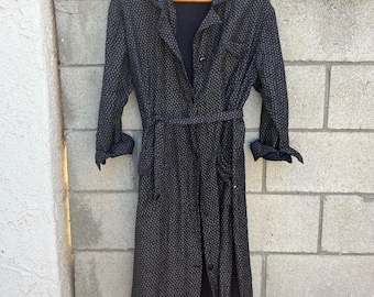 May include: A dark grey patterned trench coat with a matching belt, hanging on a wooden hanger. The coat features a button-down front, long sleeves, and pockets. The fabric has a subtle, repeating pattern.