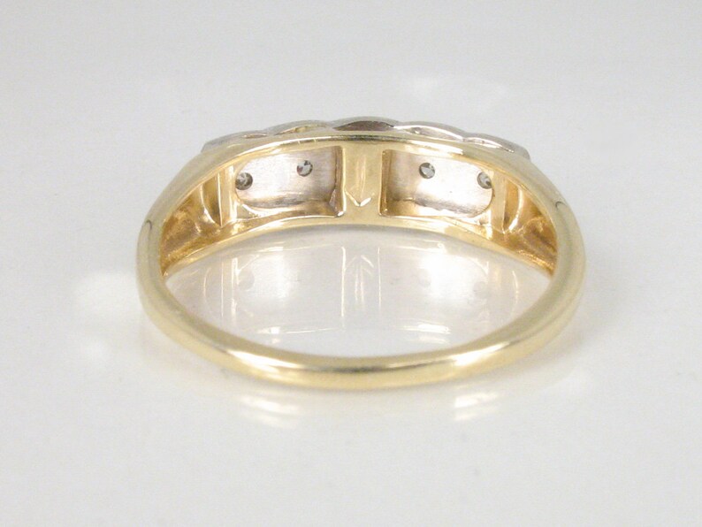 Puede incluir: Un anillo de banda de oro con tres peque&ntilde;os diamantes engastados en la banda. El anillo est&aacute; hecho de oro de dos tonos, con una banda de oro amarillo y detalles de oro blanco.