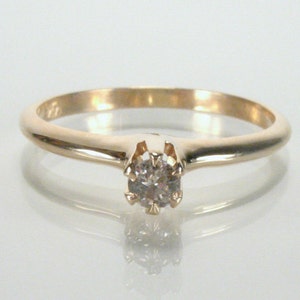 May include: A simple gold band ring with a single round diamond set in a prong setting.
