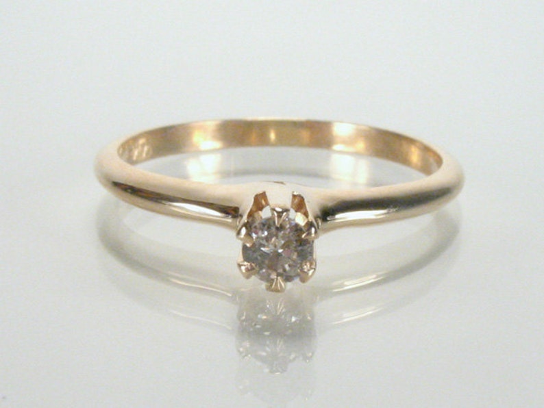 May include: A simple gold band ring with a single round diamond set in a prong setting.