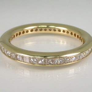 May include: A gold band ring with a row of small, square-shaped diamonds set in the band.