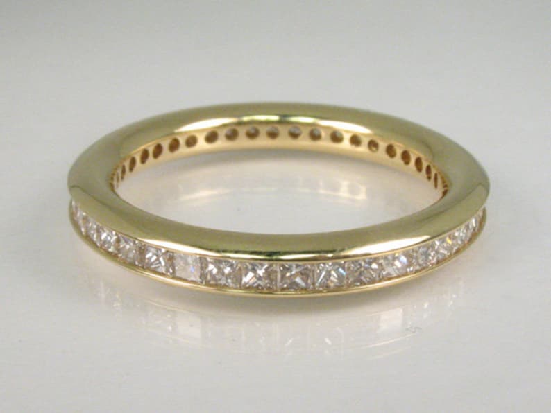May include: A gold band ring with a row of small, square-shaped diamonds set in the band.