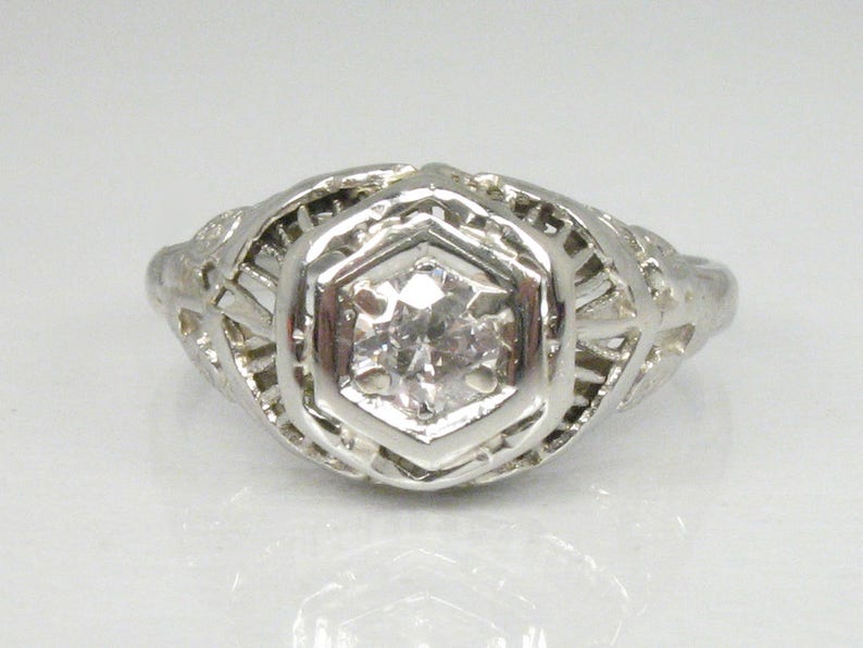 May include: A silver filigree ring with a single round diamond in the center.