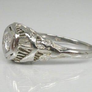 May include: A silver ring with a large, clear gemstone set in a filigree design. The ring has a delicate, intricate design with floral motifs.