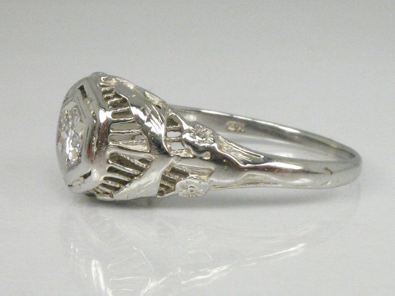 May include: A silver ring with a large, clear gemstone set in a filigree design. The ring has a delicate, intricate design with floral motifs.