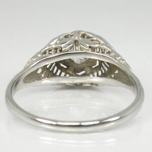 May include: A silver filigree ring with a clear stone in the center. The ring is delicate and intricate, with a floral design.