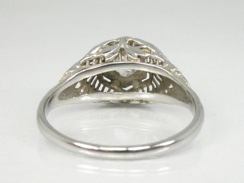 May include: A silver filigree ring with a clear stone in the center. The ring is delicate and intricate, with a floral design.