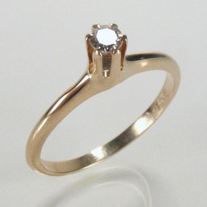 May include: A simple gold band ring with a single, small, round diamond set in a four-prong setting.