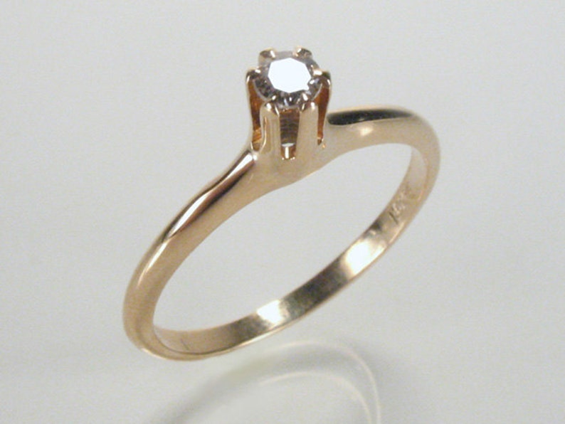 May include: A simple gold band ring with a single, small, round diamond set in a four-prong setting.