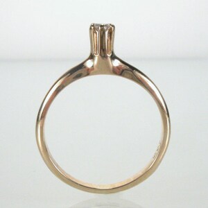 May include: A simple gold band ring with a single, small, clear gemstone set in a prong setting.