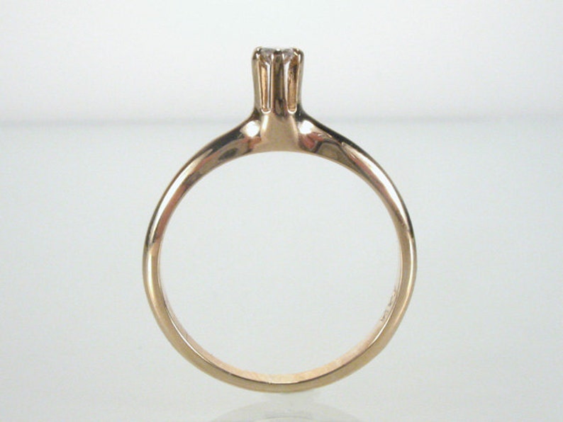 May include: A simple gold band ring with a single, small, clear gemstone set in a prong setting.