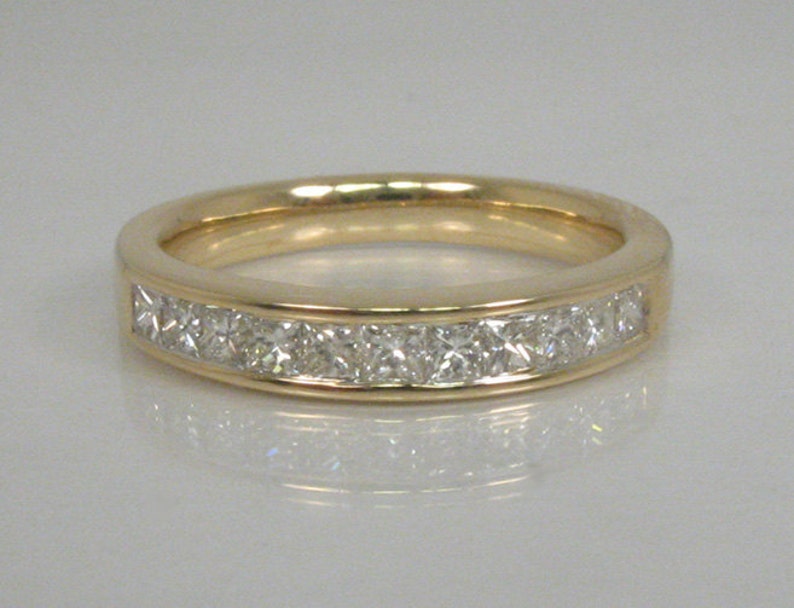 May include: A gold band ring with a row of small, square-shaped diamonds set in a channel setting.