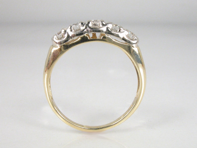 Puede incluir: Un anillo de banda de oro con cinco diamantes redondos engastados en fila.