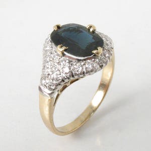 May include: A gold ring with a large oval-shaped blue sapphire surrounded by a halo of smaller diamonds.