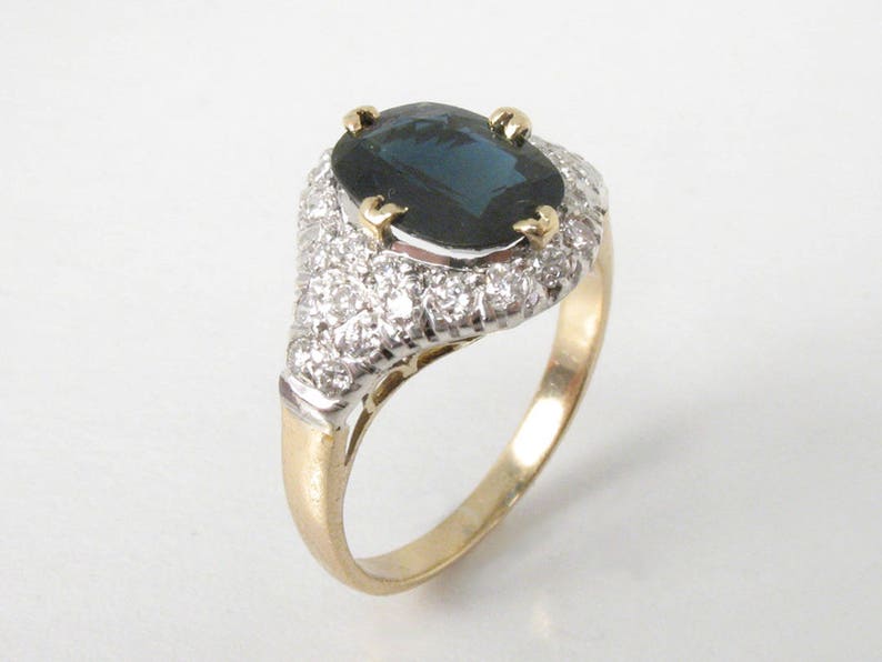 May include: A gold ring with a large oval-shaped blue sapphire surrounded by a halo of smaller diamonds.