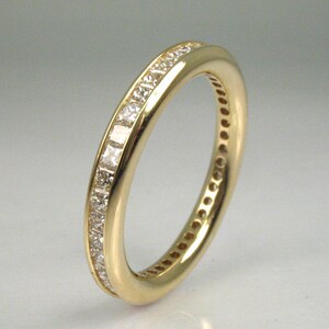May include: A gold band ring with a row of small, clear, square-shaped diamonds set in a channel setting.