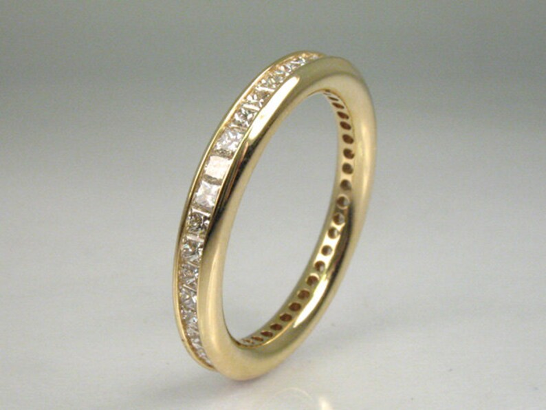 May include: A gold band ring with a row of small, clear, square-shaped diamonds set in a channel setting.