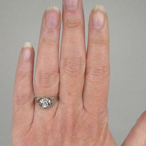 May include: A silver ring with a round, clear stone set in a filigree design.