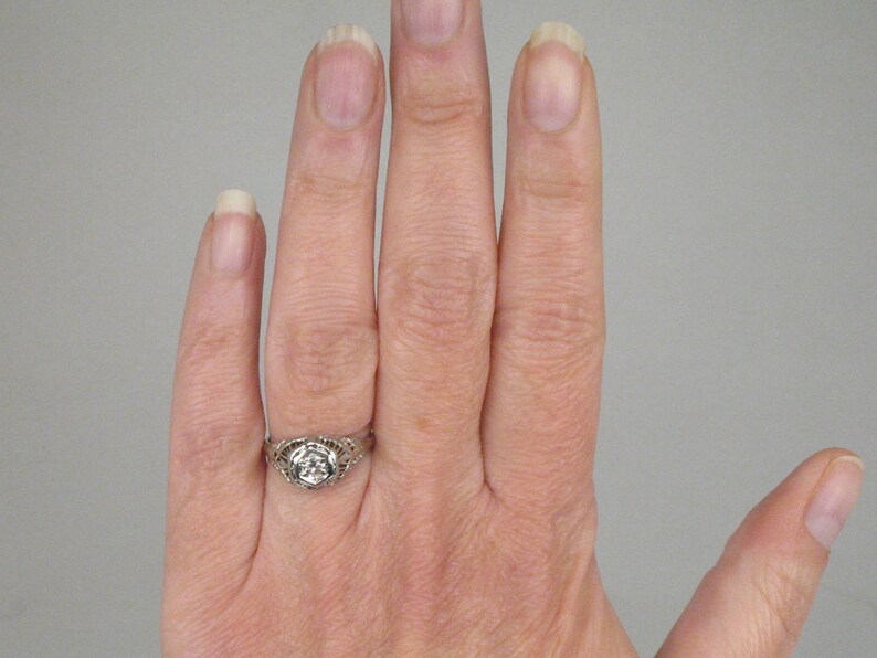 May include: A silver ring with a round, clear stone set in a filigree design.
