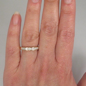 May include: A gold band with a row of small, square-shaped diamonds.