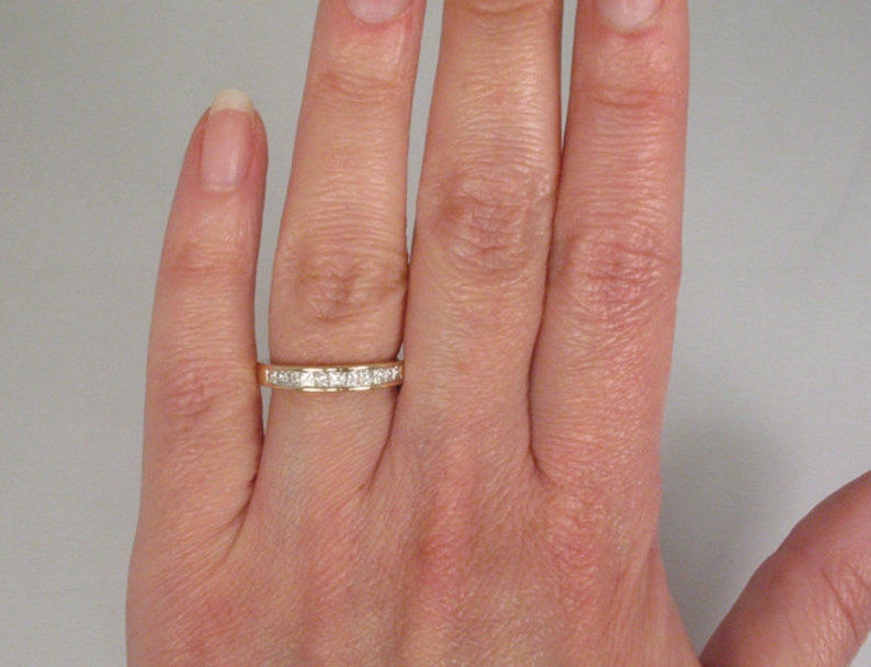 May include: A gold band with a row of small, square-shaped diamonds.